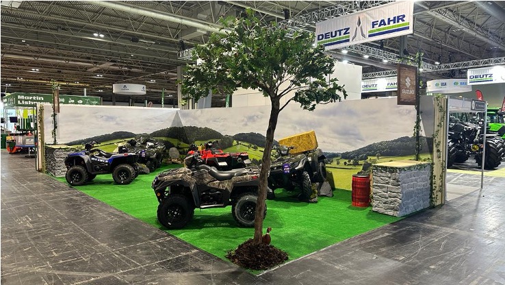 An exhibition stand with fake grass flooring, several ATVs and background graphics that look like the english countryside.