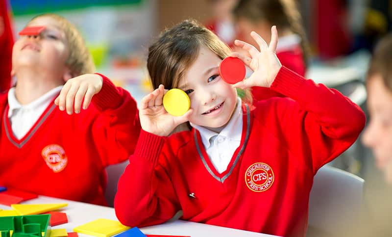 School child holding up coloured round discs over her eyes